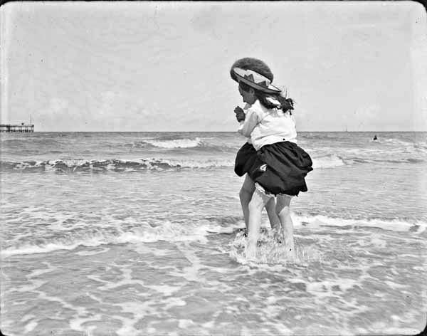 Two girls playing in shallow water at the seaside with backs to the camera