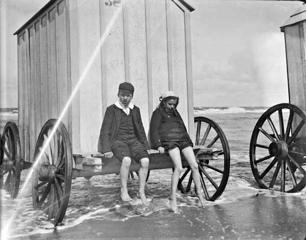 Young girl and boy sitting on a bathing box, in shallow water