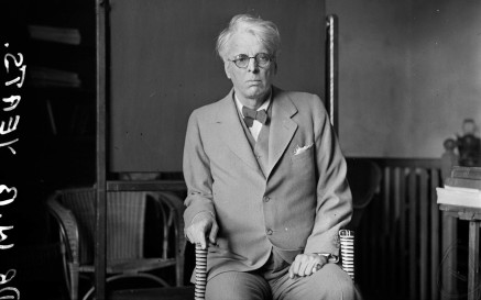 WB Yeats wearing a suit, seated in a chair and leaning slightly on a cane 