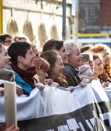 A number of women holding up a large banner