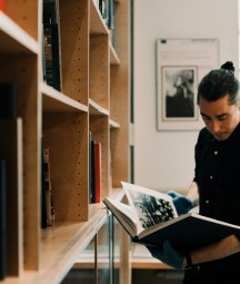 A male librarian consults a large book beside a book shelf