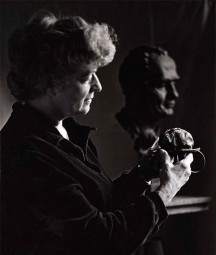 A black and white photo of Helen Hooker O'Malley holding a sculpture, with a bust in the background woman 