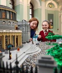 Acting Director Katherine McSharry and child standing next to the front of Lego model of NLI