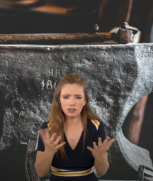 A white woman interpreting a poem. The background image is of an anvil in a blacksmith's forge. 