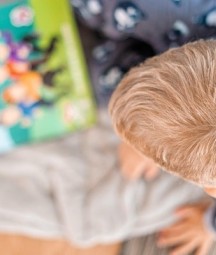Picture from above of a child with blonde hair looking at a colourful story book. 