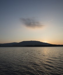 Photograph of low sun on Belfast lough. Water the foreground and a mountain in the distance.
