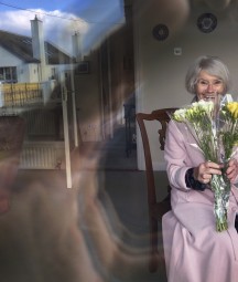 Older woman behind window holding a bunch of flowers