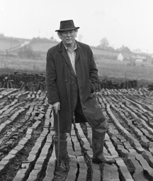 Seamus Heaney standing in the bog leaning on a wooden walking stick