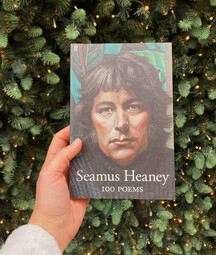 A hand holding up Heaney's 100 poems in front of Christmas lights