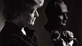 A black and white photo of Helen Hooker O'Malley holding a sculpture, with a bust in the background woman 