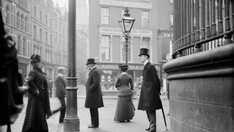 Men and women of Dublin stand on the footpath at the junction of Suffolk Street, Grafton Street and Nassau Street. 