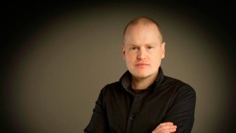 Photograph of a white man in a black jumper.