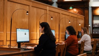 three women sit researching at computer screens inside of the NLI's main reading room