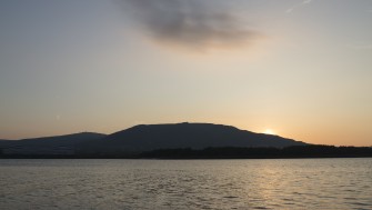 Photograph of low sun on Belfast lough. Water the foreground and a mountain in the distance.