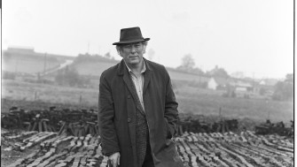 Black and white photo of man standing at turf bog. 
