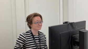 Photograph of woman with glasses on looking at a computer. 