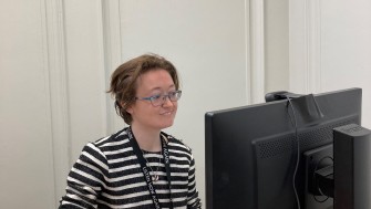 Photograph of woman with glasses on looking at a computer.