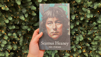 A hand holding up Heaney's 100 poems in front of Christmas lights