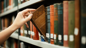 hand reaching for a book on a library shelf