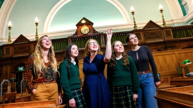 NLI Acting Director Katherine McSharry surrounded by four young women, gesturing with her hand in the NLI Main Reading Room