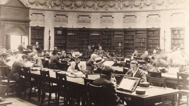 A sepia photo featuring men and women sitting at the desks in the interior of the Reading Room, 1880-1900