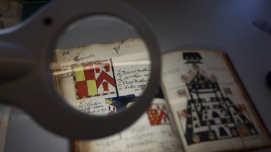 Photograph of magnifying glass hovering over an open manuscript (Funeral Entries Vol. 1, 1588-1617)