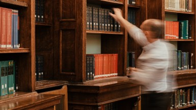 A blurred image of a man replacing a book on a shelf in the NLI Main Reading Room