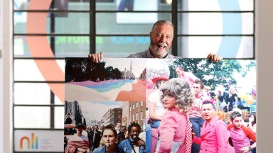 A man holds up an enlarged photograph of a Pride parade