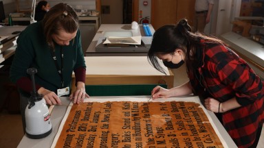 Two people working on conserving an old poster
