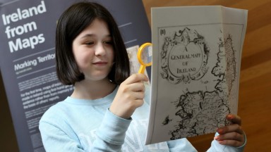 A young girl uses a yellow magnifying glass to examine a historic map. 