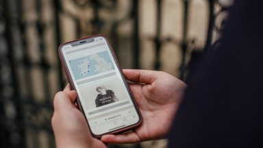 Hands holding phone at library gate with nli catalogue on screen