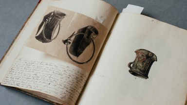 Íomhá de leabhar oscailte le líníochtaí agus scríbhneoireacht