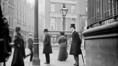 Men and women of Dublin stand on the footpath at the junction of Suffolk Street, Grafton Street and Nassau Street. 