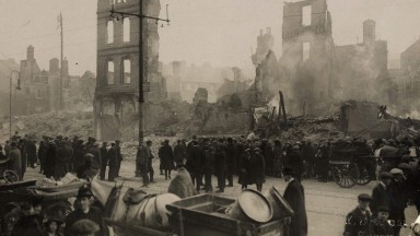 A black and white photograph shows citizens standing in ruins of Patrick Street, Cork after the burning of Cork.