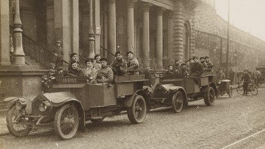 Grianghraf dubh agus bán de dhá ualach carranna na nDúchrónach ag fágáil foirgnimh ar Shráid Amiens 