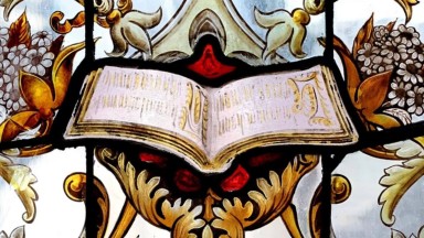 A portion of stained glass featuring an open book surrounded by ornate decorations 