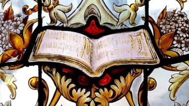 A portion of stained glass featuring an open book surrounded by ornate decorations