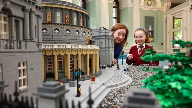 An Stiúrthóir Gníomhach Katherine McSharry agus leanbh ina seasamh in aice le tosach múnla Lego de chuid NLI