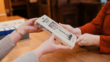 Close up photograph of two peoples hands showing an exchange of a book between a staff member with reader at Reading Room reception desk