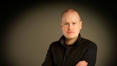 Photograph of a white man in a black jumper.