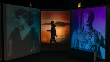 Silhouette of a boy walking behind large screens displaying Yeats' poetry inside the NLI's Yeats exhibition