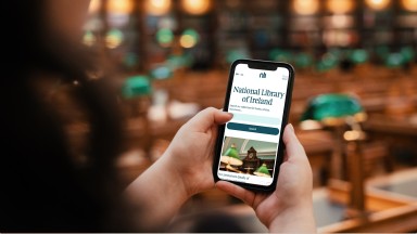 Close up a woman holding an iPhone browsing the NLI's website inside of the Reading Room