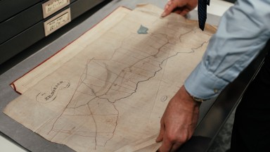 man handling a historical map laid out on a table 
