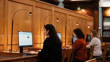 three women sit researching at computer screens inside of the NLI's main reading room