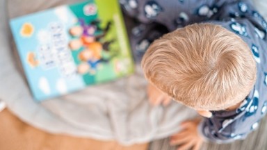Picture from above of a child with blonde hair looking at a colourful story book. 