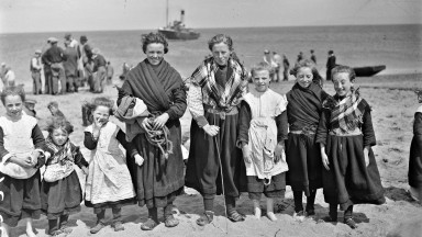 Black and white photograph of a group of women and children on a beach on the Aran Islands wearing traditional clothes