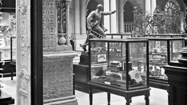 Interior black and white photograph of the National Museum in Dublin with exhibition cases and statues on display