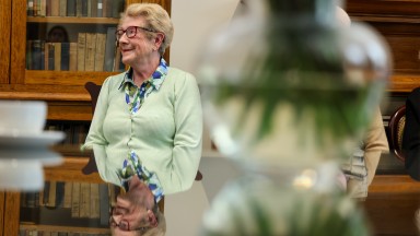 Woman sitting at a table smiling with vase of flowers in foreground