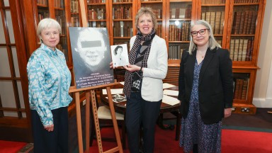 Three women standing next to a poster on a easel and one holding a black and white photography