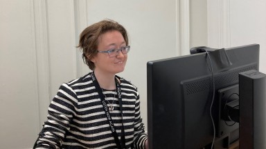 Photograph of young woman with short brown hair and glasses looking at computer screen. 